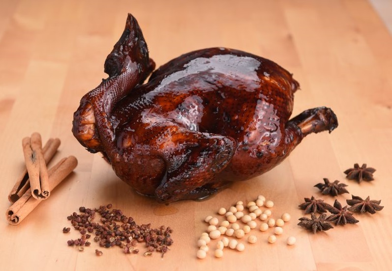 Whole soy sauce chicken glazed in dark soy, surrounded by star anise, cinnamon sticks, peppercorns and soybeans
